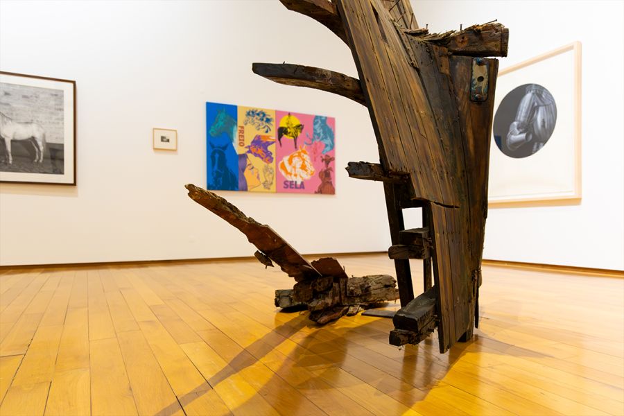 Escultura de madeira numa sala de exposição com quadros na parede