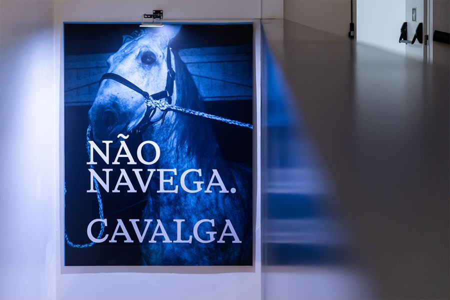 Cartaz com um cavalo e a frase «Não navega. Cavalga.» numa exposição
